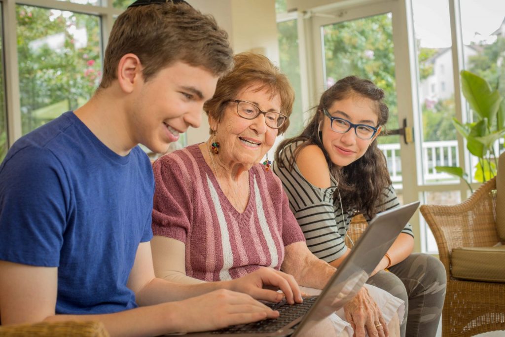 Young Adults sitting with elderly lady on couch on computer donating to Charles E. Smith Life Communities