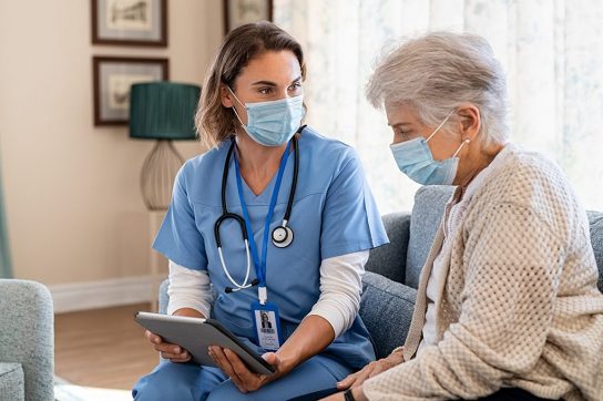 Nurse chatting with senior woman, both are wearing masks.